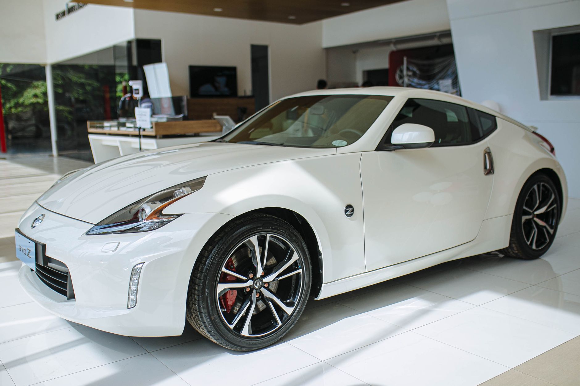 Ilustrasi: A shiny white Nissan 370Z coupe displayed in a modern car showroom, showcasing luxury and style.