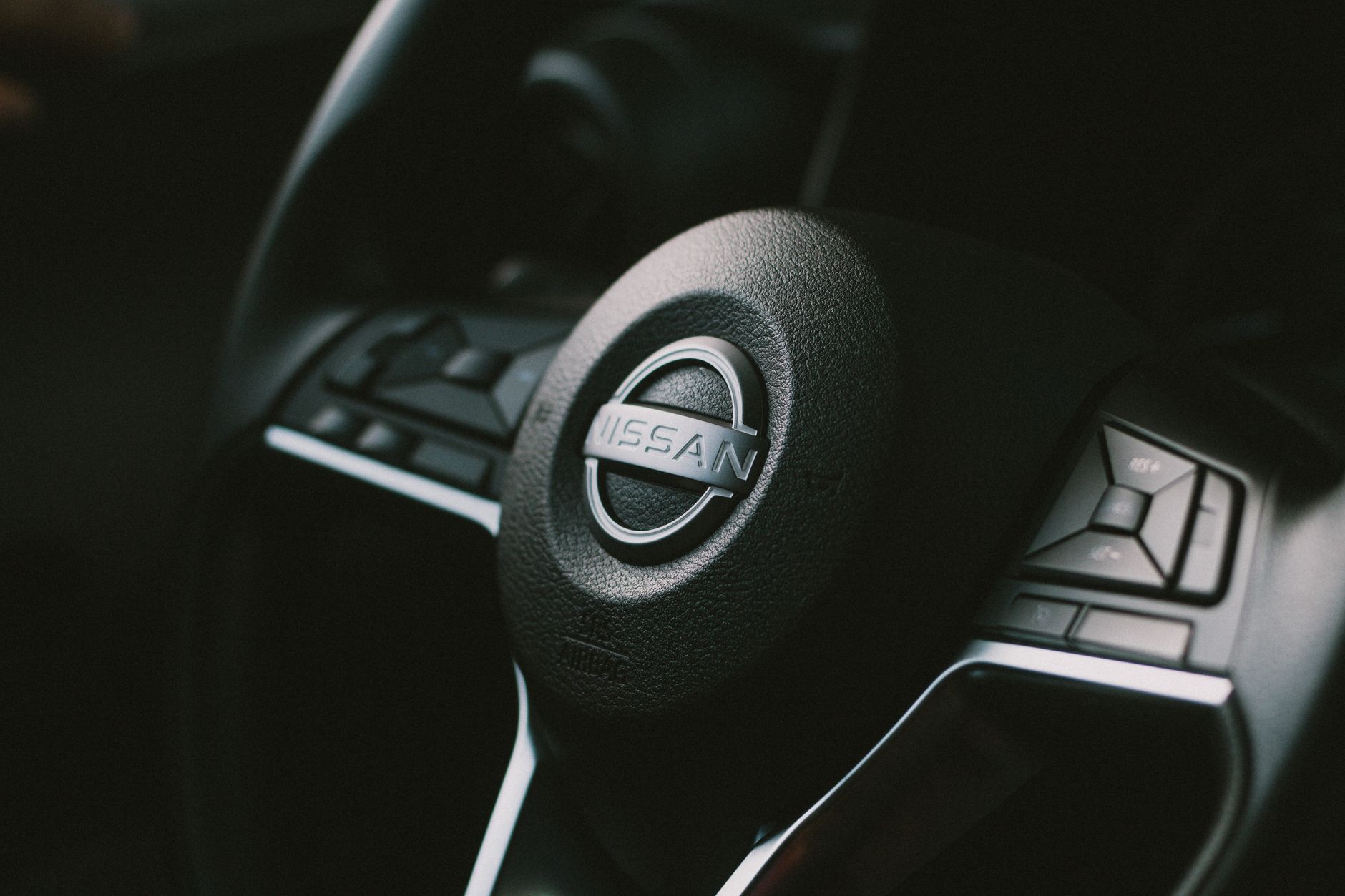 Ilustrasi: Detailed view of a Nissan steering wheel with visible controls, showcasing automotive design.