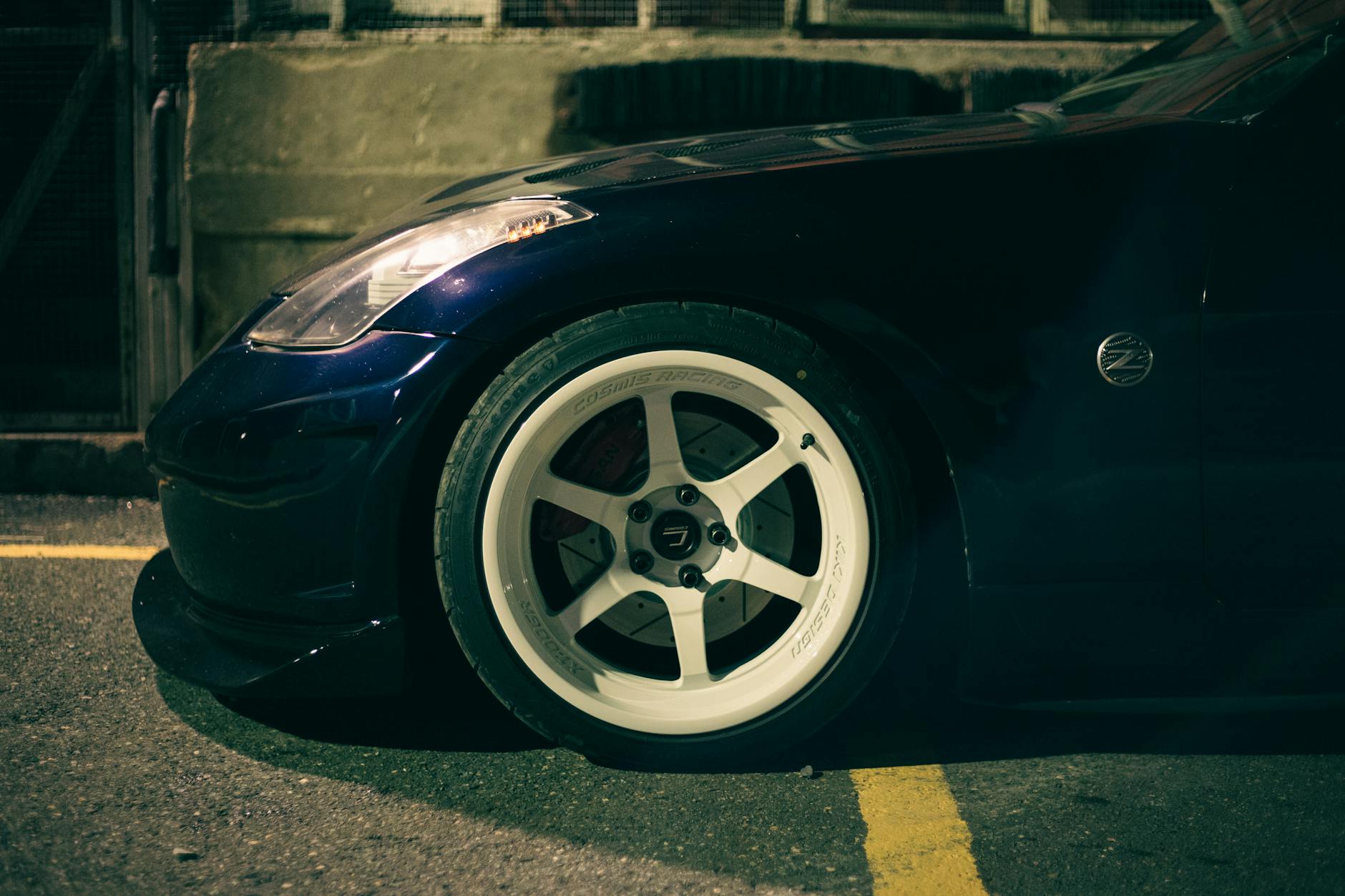 Ilustrasi: Side view close-up of a Nissan 350Z sports car wheel parked on a street malam hari, highlighting automotive details.