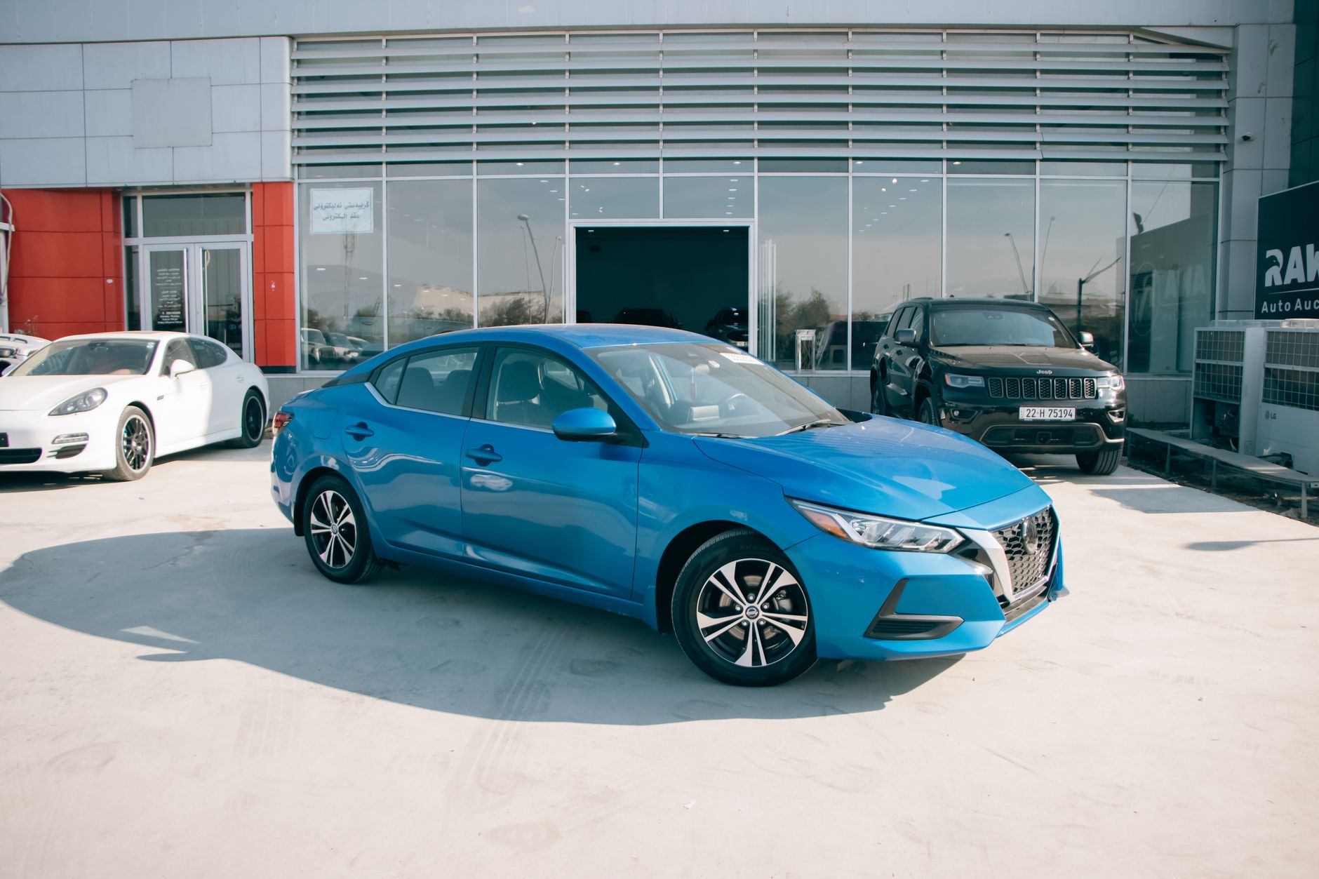 Ilustrasi: A bright blue Nissan Sentra parked in front of a car dealership on a sunny day.