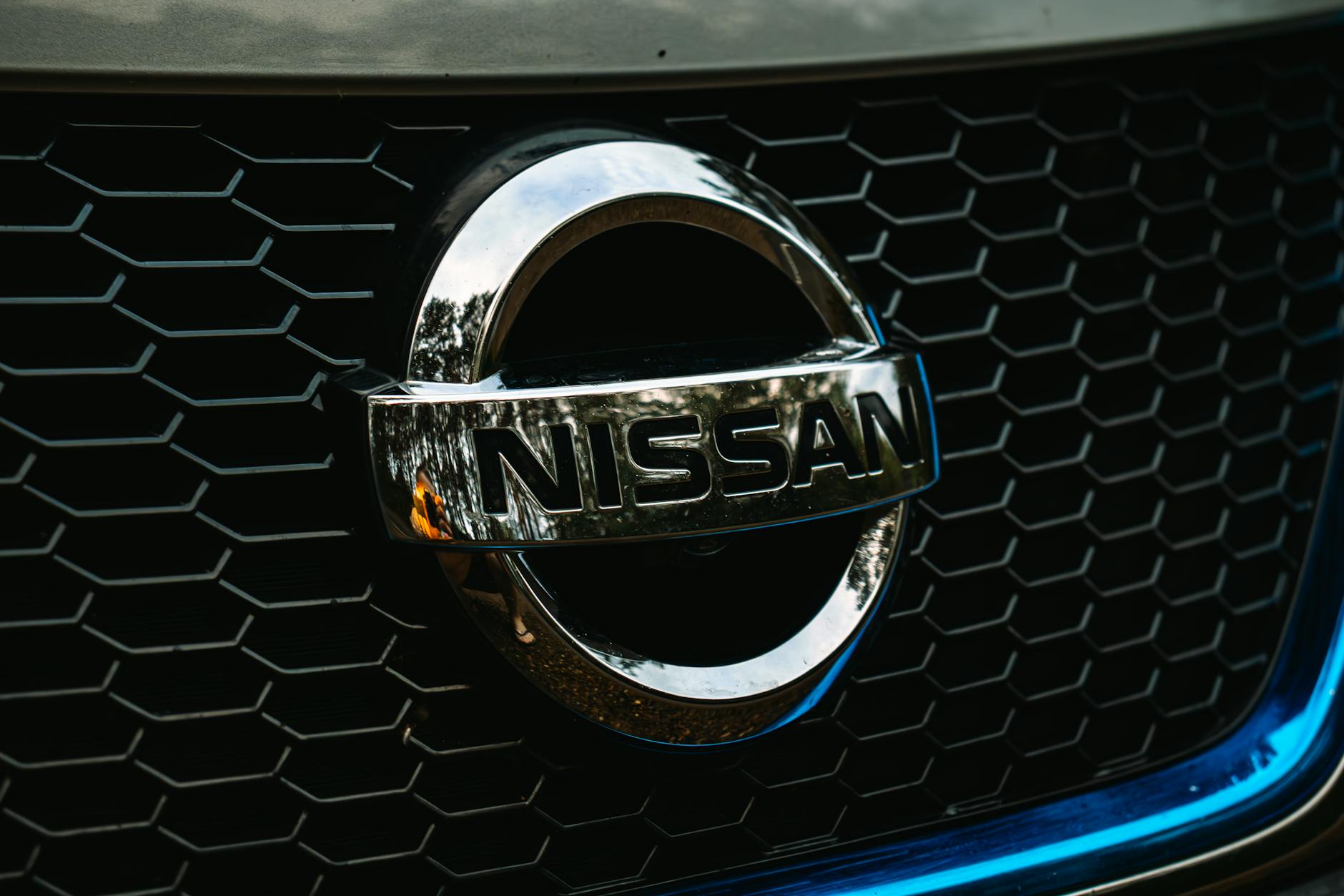 Ilustrasi: Detailed shot of the Nissan logo on a car grille grid, emphasizing automotive branding.
