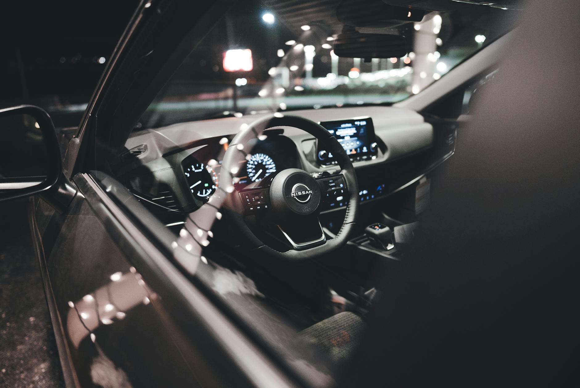 Ilustrasi: Close-up of a Nissan car's interior showing the illuminated dashboard and steering wheel malam hari.