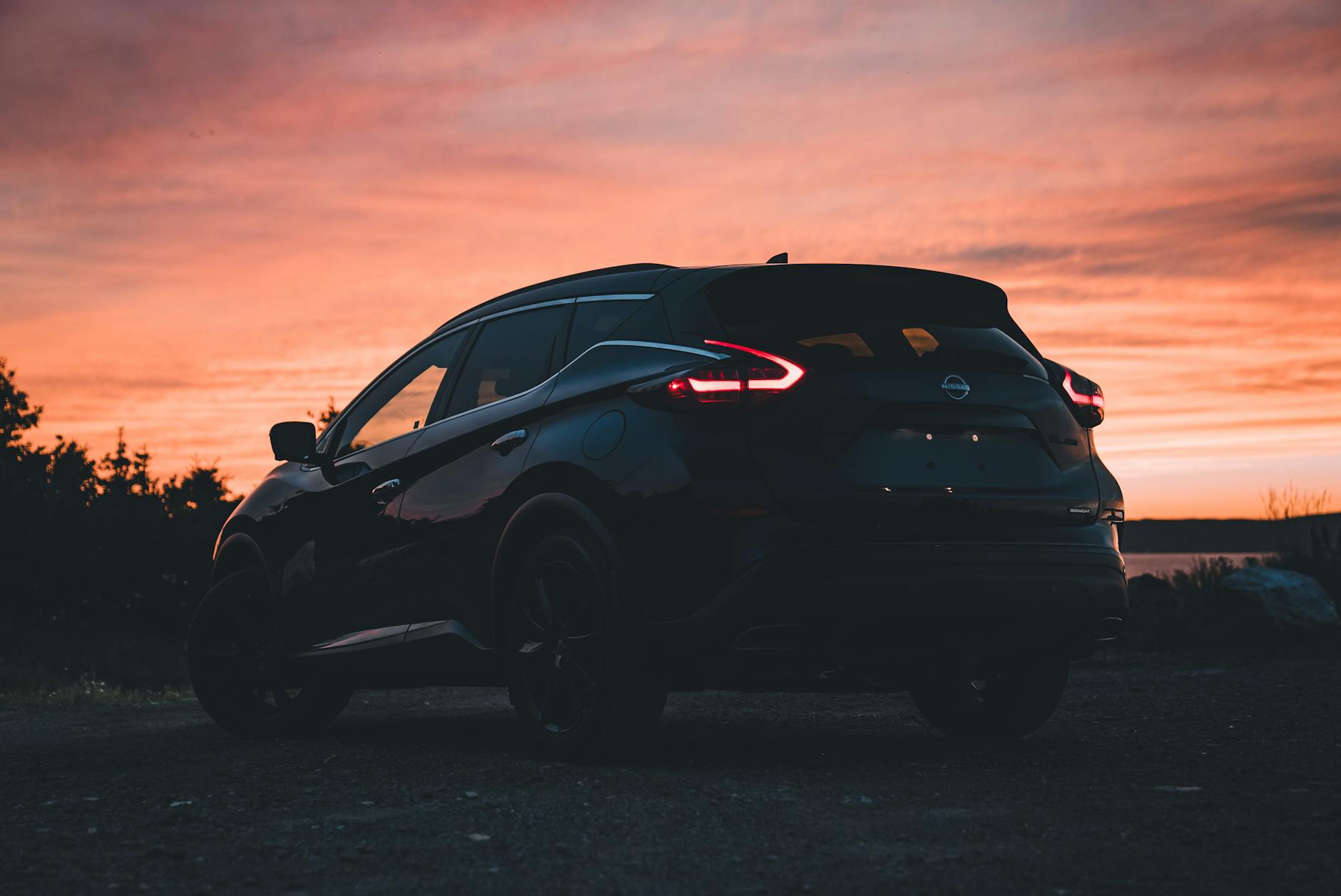 Ilustrasi: Silhouette of a Nissan Murano SUV captured at sunset, showcasing a vibrant orange sky.