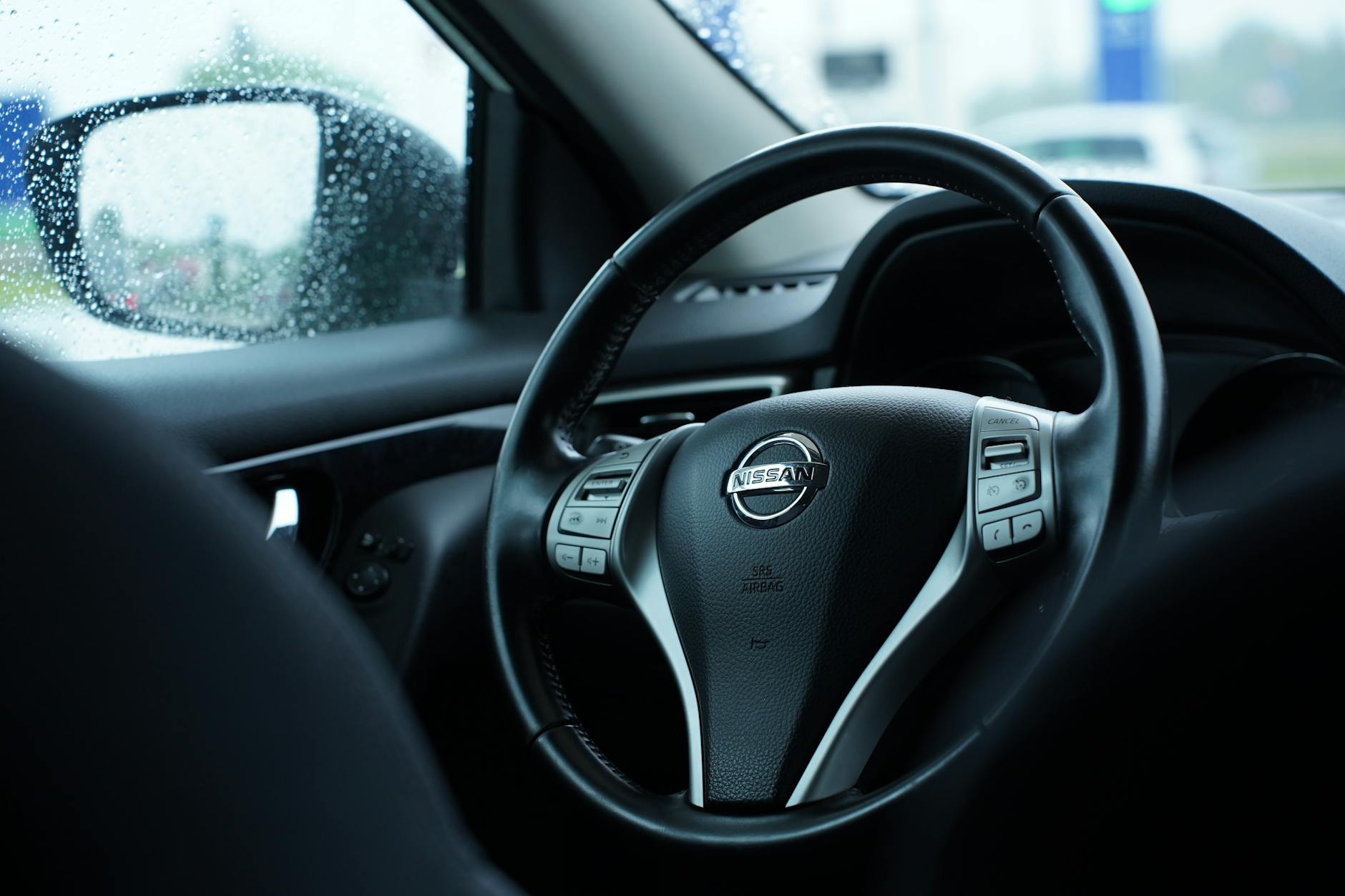 Ilustrasi: Close-up of a Nissan steering wheel in a car interior on a rainy day, showcasing sleek automobile design.