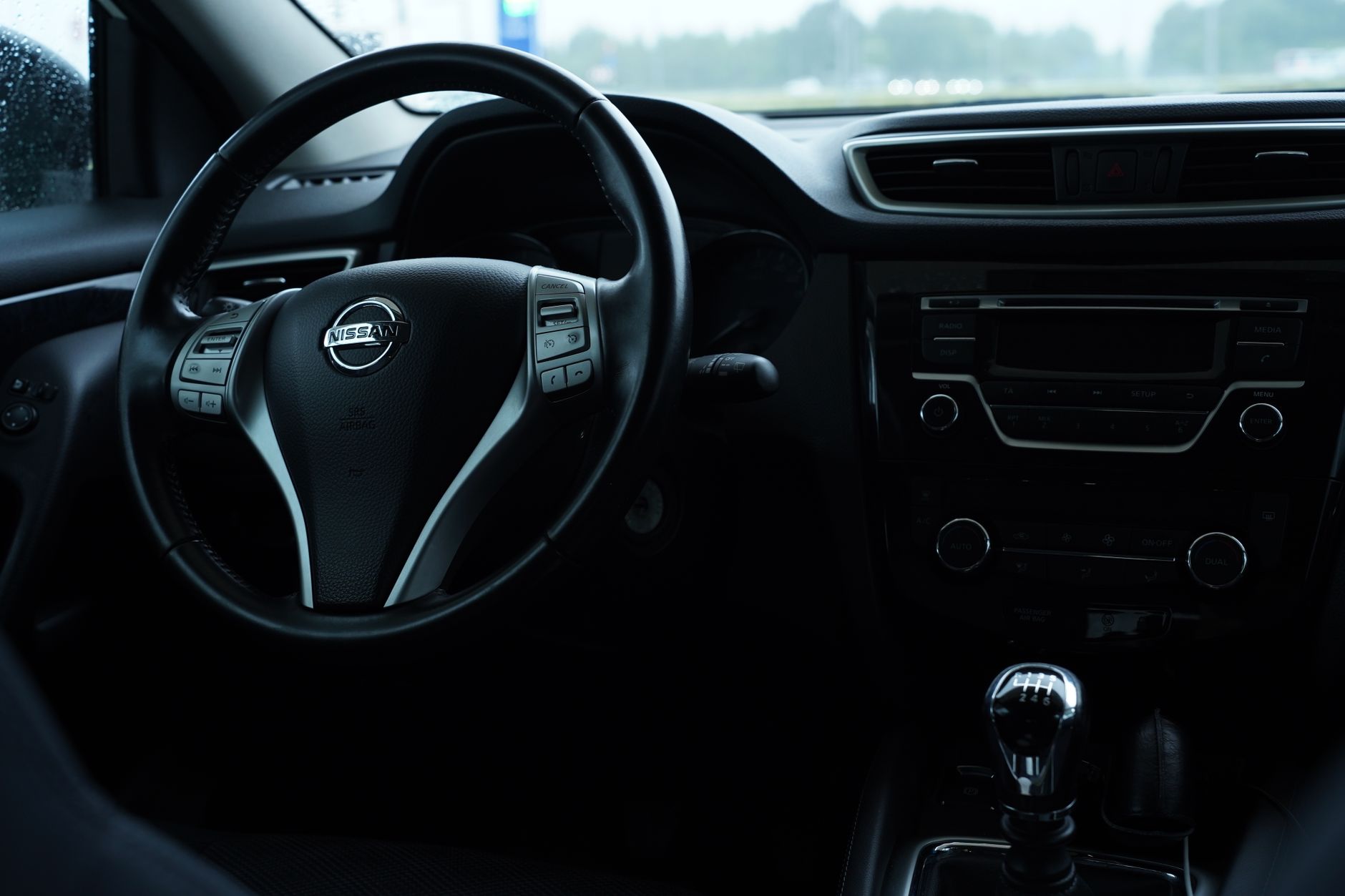 Ilustrasi: Dark interior view of a Nissan car featuring the steering wheel and dashboard details.