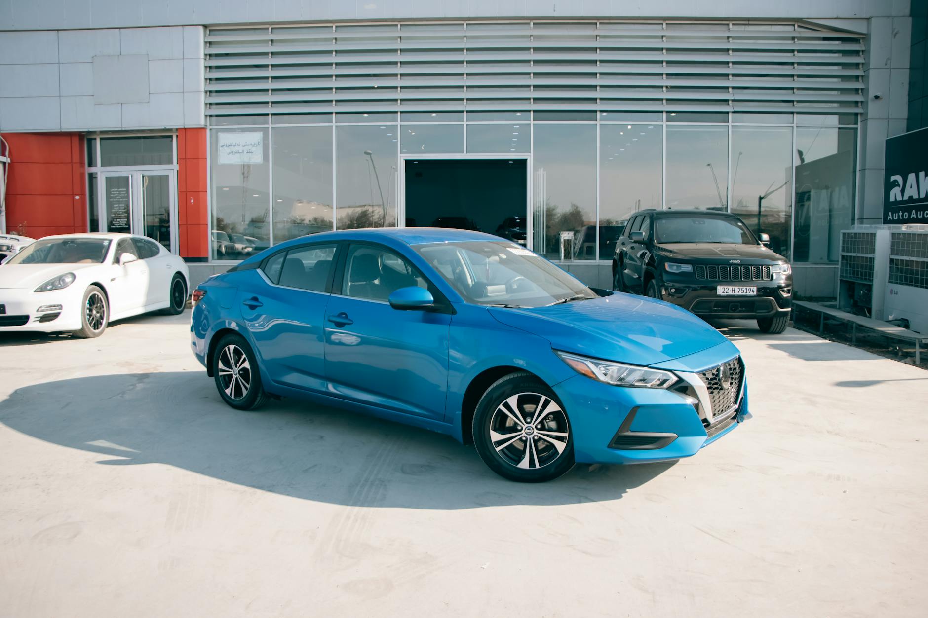Ilustrasi: A bright blue Nissan Sentra parked in front of a car dealership on a sunny day.