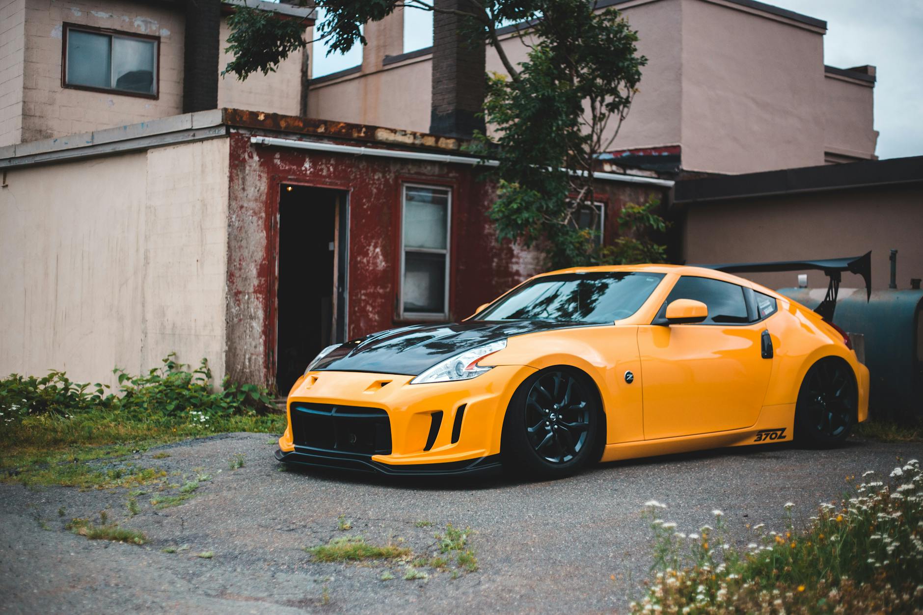 Ilustrasi: Vibrant yellow Nissan 370Z parked beside a rustic urban building, showcasing sleek design.