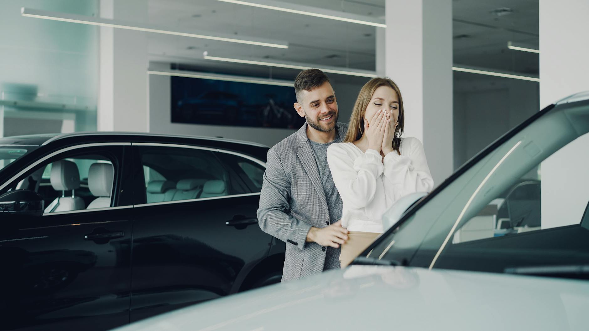 Ilustrasi: A joyful couple at a car dealership discovering their new car. Indoor setting, bright lighting.