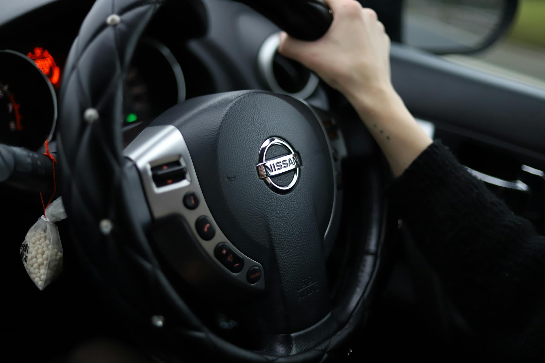 Ilustrasi: Close-up shot of a person's hand gripping a Nissan steering wheel. Modern car interior.