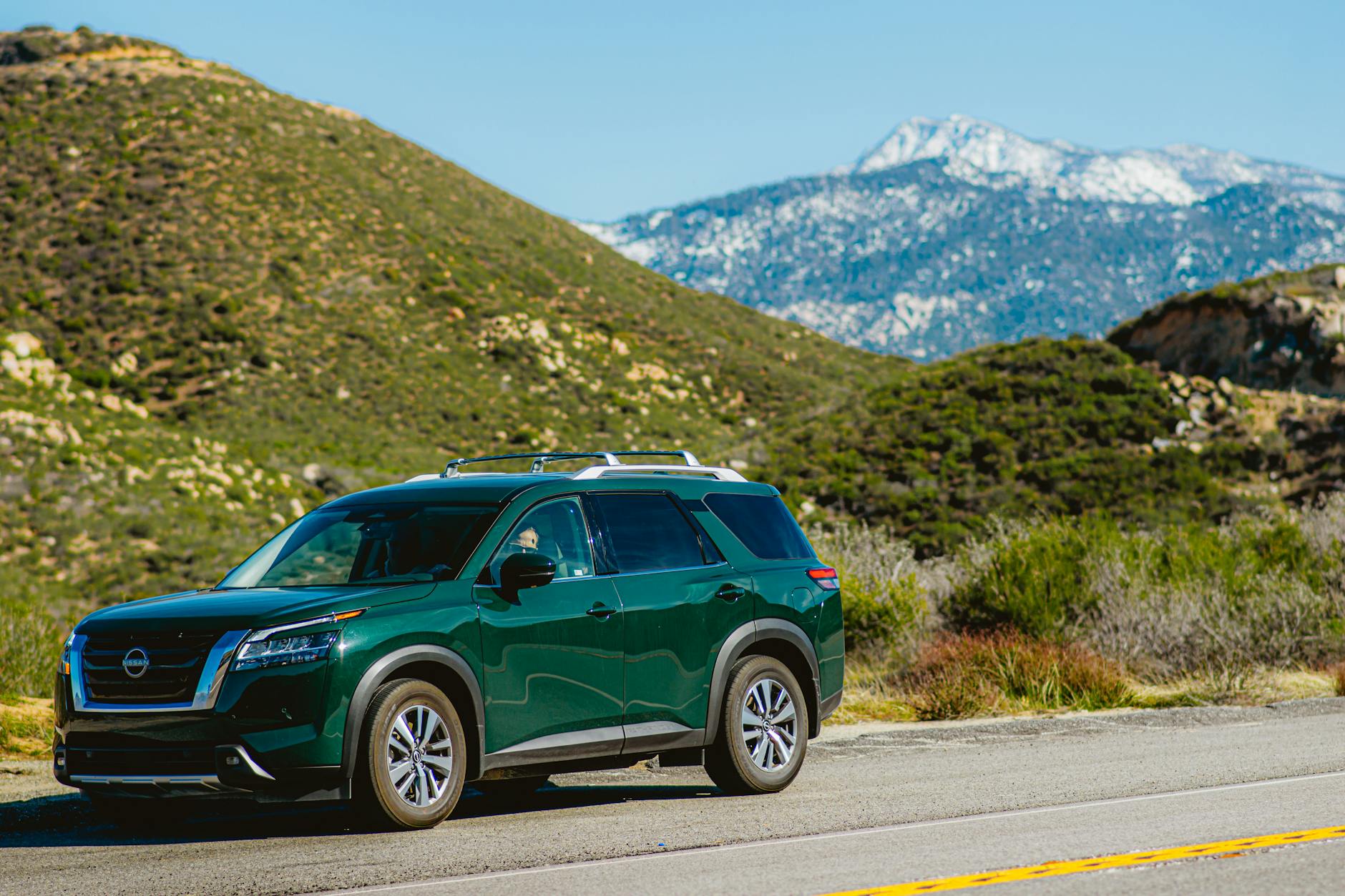 Ilustrasi: Green Nissan Pathfinder SUV on a road near lush mountains against a clear blue sky.