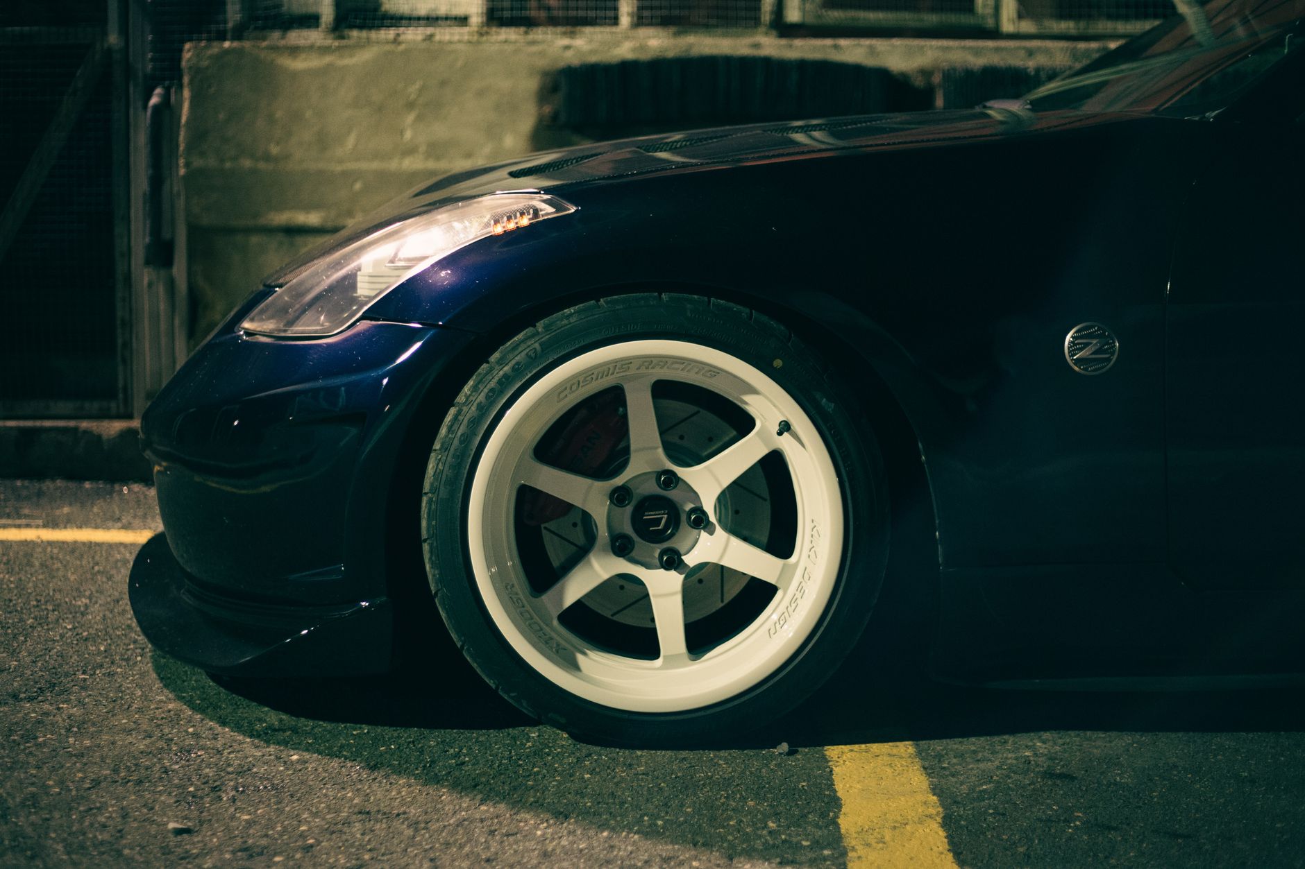 Ilustrasi: Side view close-up of a Nissan 350Z sports car wheel parked on a street malam hari, highlighting automotive details.